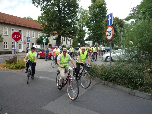 Radni i burmistrz w trakcie jazdy na rowerach dyskutują o sprawach dotyczących gminy. Urzędowy peleton widać z daleka dzięki odblaskowym kamizelkom.