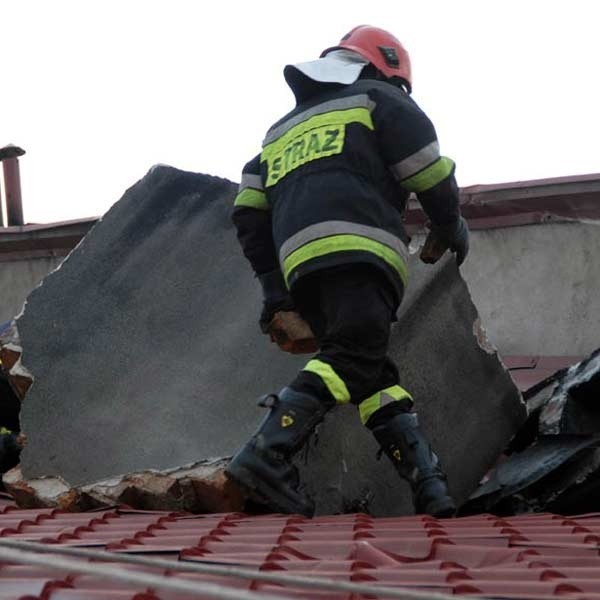 Strażacy obok przewróconego komina, który wbił się w dach.