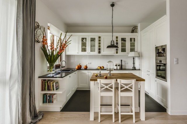 Kuchnia i jadalnia urządzone na białoStół rozdzielający kuchnię od pokoju dziennego to sposób na aranżację otwartej kuchni.