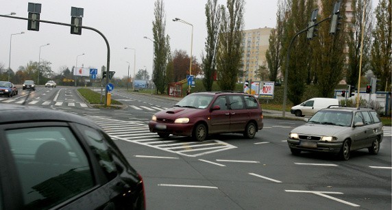 Szary opel po prawej stronie skręca w lewo korzystając z prawidłowego lewoskrętu. Czerwona kia po jego prawej stronie jedzie nieprawidłowo, kierując się wskazaniem świateł, które umożliwiają skręt i prowadzą kierowcę przez tzw. martwe pole, po którym nie wolno jeździć.