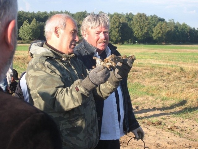Adam Sikorski z TVP INFO (z lewej) oraz kapitan PLL LOT Wojciech Tomaszewski pokazują wykopany z ziemi drążek sterowniczy samolotu  PZL P.11c.
