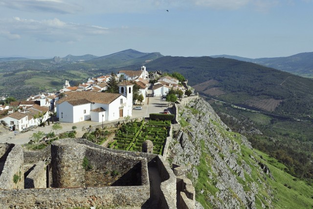 Zaledwie dwie i pół godziny jazdy od Lizbony, w wąwozie niedaleko granicy z Hiszpanią, znajduje się niewielka osada otoczona murami. To najwyżej położona wioska w Portugalii, którą zwykło określać się jako gniazdo orła ukryte w górach. Marvão, z panoramicznym widokiem na rozległe równiny regionu Alentejo, to jedno z najładniejszych miejsc w całej południowej Europie. Koniecznie trzeba zobaczyć tutejszy zachód słońca – światło odbijające się od kwarcu w granitowych głazach, które podtrzymują ogromne mury zamku, daje żywe, niemal jarzące się kolory, a także słynne fortyfikacje.– Pierwsze fortyfikacje wzniesione zostały tutaj przez Maurów w ósmym wieku. Do dziś XIII-wieczne mury zachowały się praktycznie nietknięte. Do osady prowadzi z nich wąskie, średniowieczne przejście, przy którym znajduje się ciekawie ukształtowany mauretański budynek zwany kaplicą jerozolimską. Jego wnętrze przez setki lat nie było modernizowane, nie zmieniło się tam nic. Na szczycie znajduje się piękna, niska dzwonnica z maleńką kopułą. Wyjątkowym elementem jest także piękna drewniana galeria, a na jednym z bocznych ołtarzy znajduje się niezwykły posąg Trójcy Przenajświętszej – mówi Piotr Wilk z biura podróży Rainbow.Z twierdzy zamkowej widać całą okolicę – leżące na południu Serra de São Mamede i urocze miasto Estremoz, na północy góry Serra da Estrela (góry Gwiazd) z Castelo de Vide na północnym zachodzie, a na północnym wschodzie, za horyzontem roztacza się już Hiszpania. Źródło: r.pl