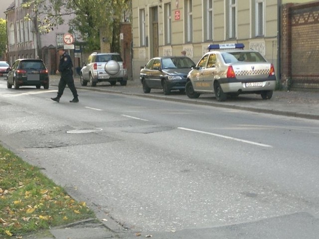 Na zdjęciu widać jak fukcjonariusz idzie przez ulicę.
