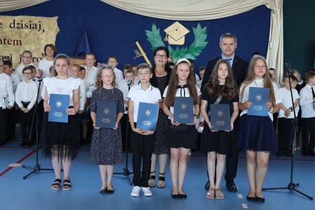 Burmistrz Paweł Wójcik oraz wiceprzewodnicząca rady Teresa Chwalińska wraz z uczniami, którzy otrzymali stypendia podczas zakończenia roku szkolonego w chmielnickiej podstawówce.