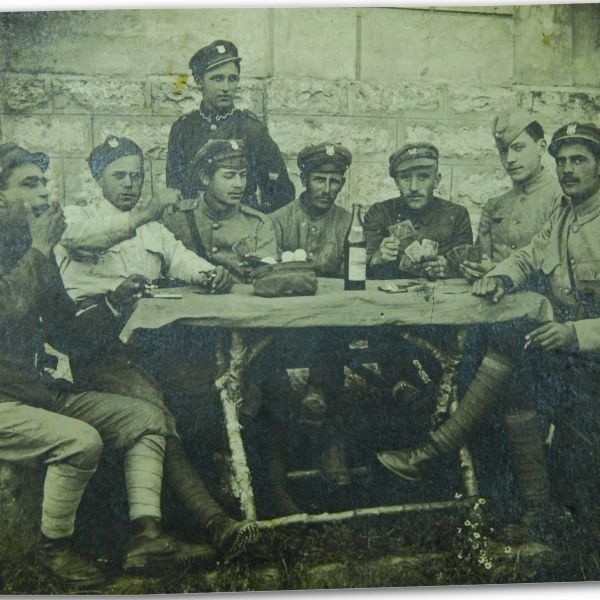 Grupa legionistów podczas spotkania wielkanocnego w 1919 roku, po bitwie z bolszewikami pod Baranowiczami. Uśmiechnięte twarze, świąteczny nastrój. Na stole polowym są jajka i butelka "okowity". Krążą kieliszki i toczy się gra w karty. Pierwszy z lewej z organkami przy ustach to właśnie Władysław Falkowski.