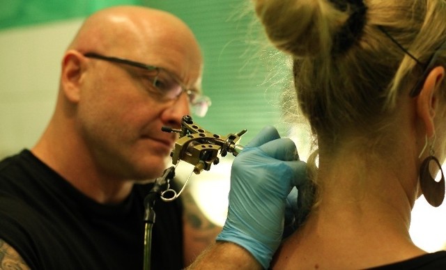 Robert Cieślak wykonuje tatuaż za uchem klientki. 