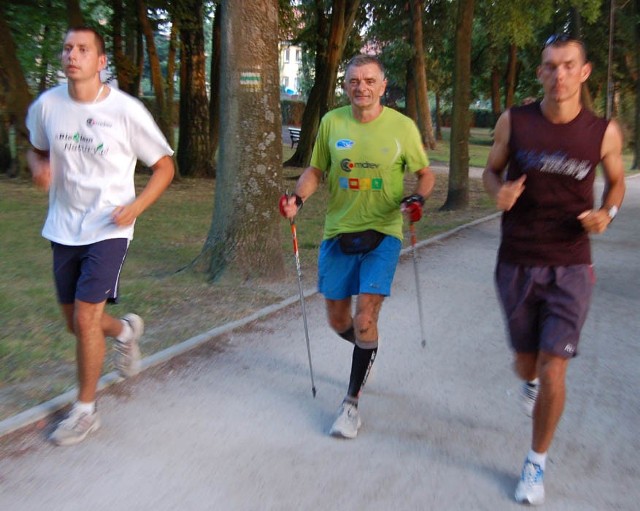 Andrzej Kowal w asyście dwóch biegaczy pokonuje parkowe alejki. 