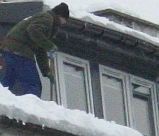 Odśnieżanie dachu niesie wiele zagrożeń. Ten mężczyzna jest asekurowany specjalnym pasem.