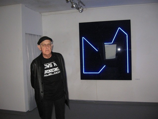 Zbigniew Gostomski na tle swoich prac ze "świecących neonów&#8221; z cyklu "Dom&#8221;.