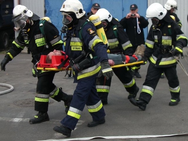 Strażacy wynoszą poszkodowaną osobę w pożarze zakładowego magazynu opakowań.