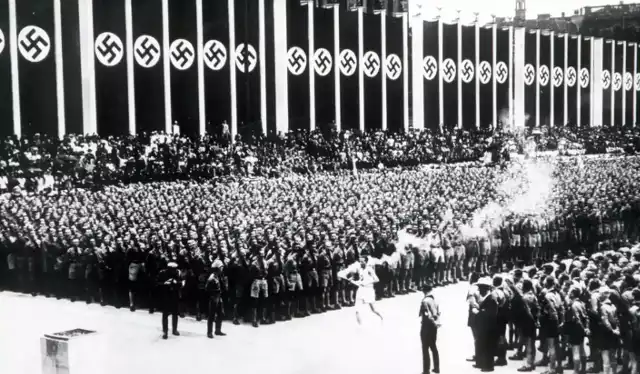 Znicz olimpijski przybywa na Stadion Olimpijski w Berlinie otoczony ogromnymi nazistowskimi flagami ze swastyką w 1936 roku