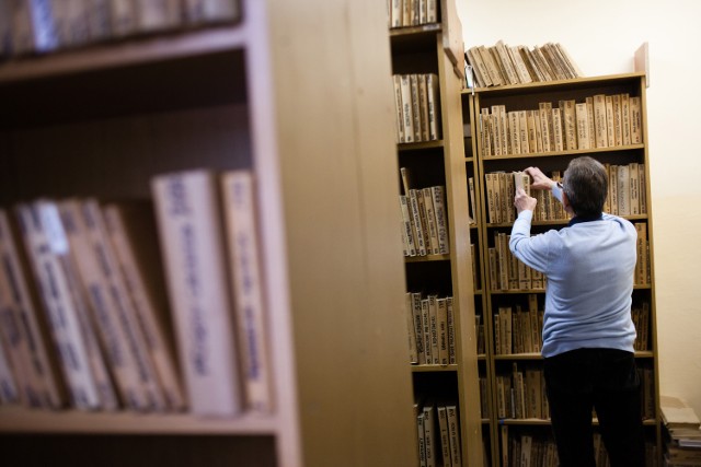 67-letni Marian C. podczas dyżuru w zakładowej bibliotece porządkuje książki na półkach