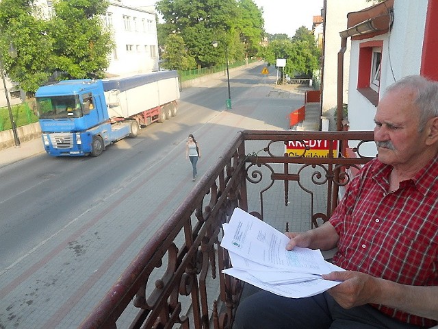 Lucjan Kacprzak ze swojego balkonu obserwuje ruch ciężarówek. W ręku trzyma kopie pism wysłanych w  tej sprawy
