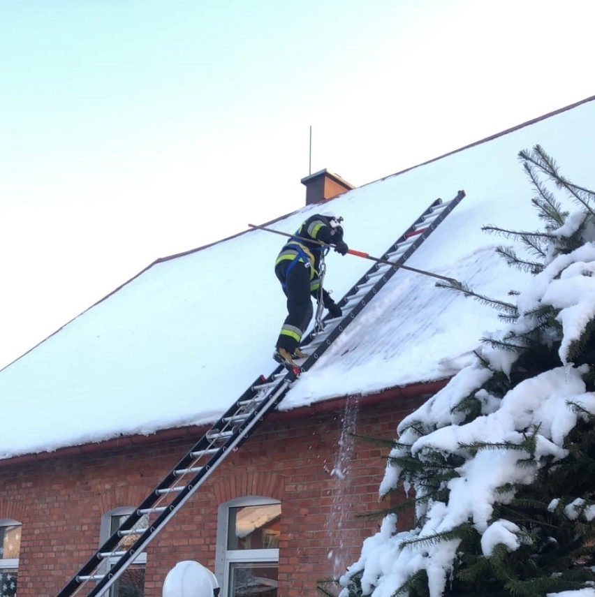 Zwisające sople i zgromadzony na dachu szkoły śnieg w...