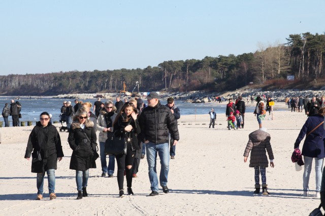 Już bez czapek, ale za to w okularach słonecznych, turyści spacerują po plaży.