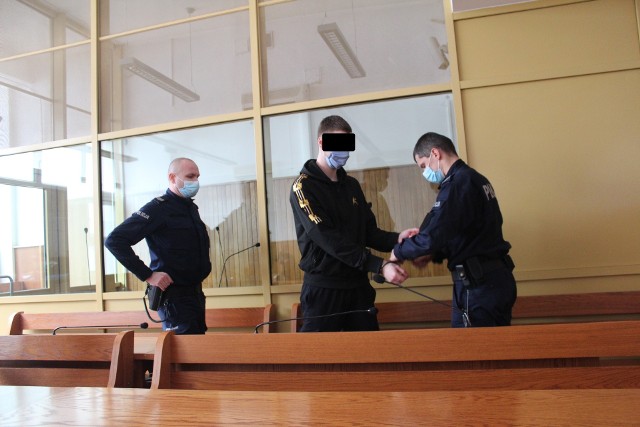 Adrian C. przed krakowskim sądem w  konwoju policyjnym. usłyszał wyrok 3 lat więzienia za próbę rozboju z nożem.