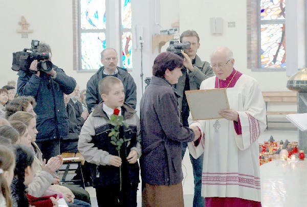 Stanisława Ścigacz wraz z wnuczkiem odbiera  dyplom z rąk ks. infułata Tadeusza Nowickiego.