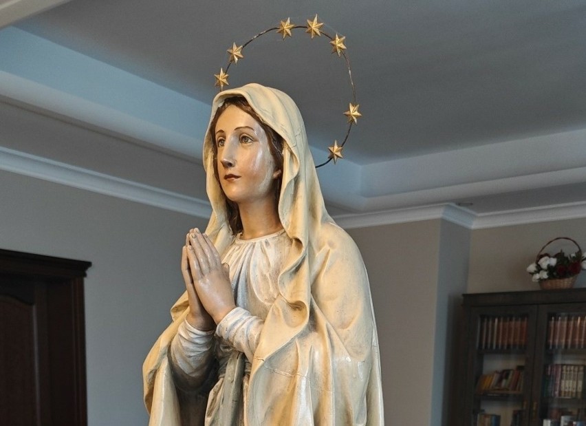 Rzeźba przedstawia postać Matki Bożej ze złożonymi dłońmi w...