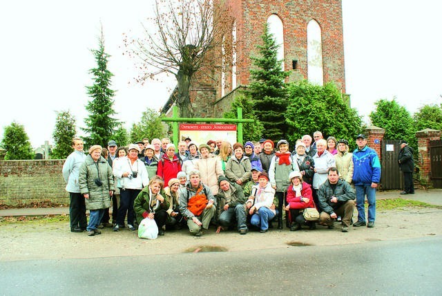 Uczestnicy wycieczki PTTK przed kościołem w Ostrowitem. Miejscowość jest stolicą Kosznajderii, o czym informuje stosowna tablica.