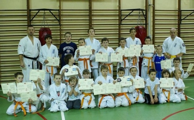 Pamiątkowe zdjęcie młodych karateków z certyfikatami z egzaminów i międzynarodowymi legitymacjami.