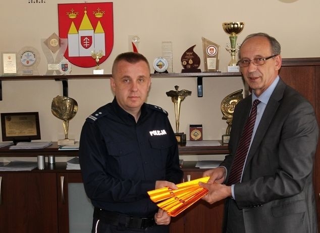 Wójt Stanisław Herej przekazuje komendantowi policji Mariuszowi Przyborowskiemu opaski odblaskowe.