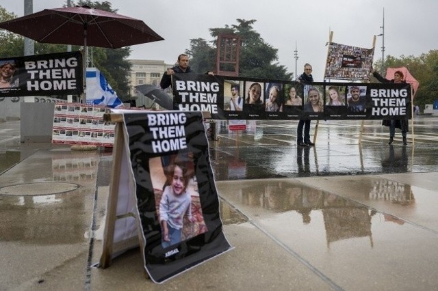 Protestujący trzymają transparent ze zdjęciami zakładników wziętych przez Hamas z południowego Izraela podczas zgromadzenia obok europejskiej siedziby Organizacji Narodów Zjednoczonych w Genewie.