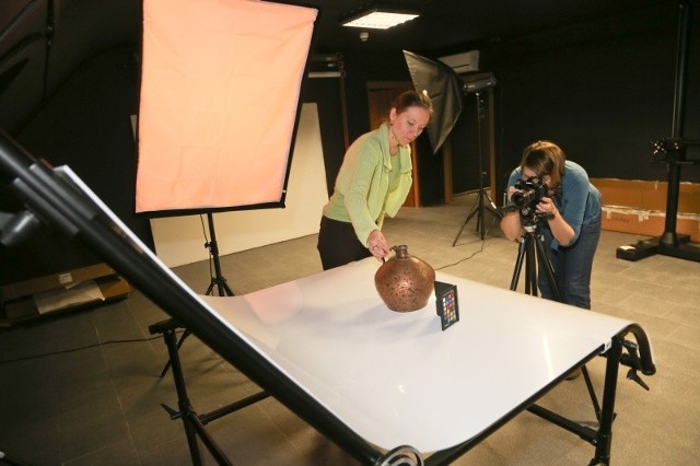 Monika Więcław, pracownica Muzeum Podlaskiego stawia na stole bezcieniowym dawne naczynie, a Anna Sierko-Szymańska fotografuje eksponat. Zdjęcie znajdzie się na stronie internetowej.