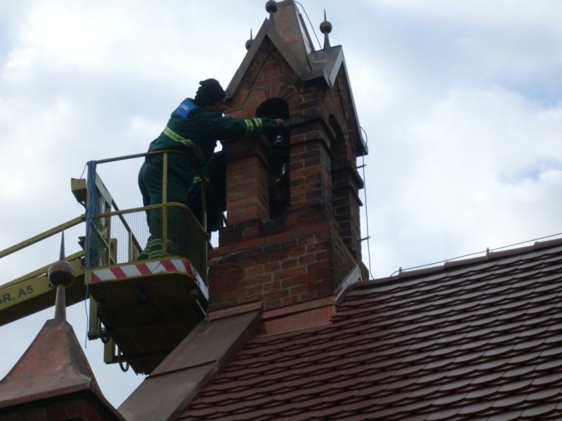 Pracownicy montują dzwon na wiezy kaplicy.