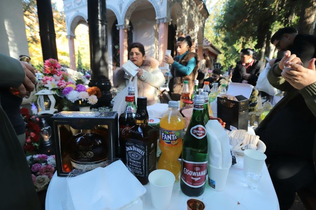 Romska biesiada przy grobach na cmentarzu Osobowickim. Stoły przy grobach zastawione są jedzeniem. Nie brakuje kiełbasy, wódki i innych alkoholi