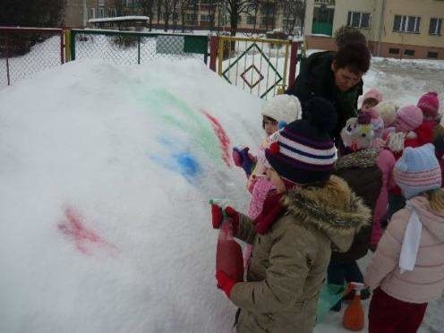 Przedszkolaki malują farbami kolorowe kwiaty na śniegu
