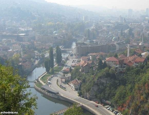 Nad Sarajewem górują strzeliste wieże minaretów, wybijające się spośród czerwonych dachów domów. Przez centrum wije się rzeka Miljacka.