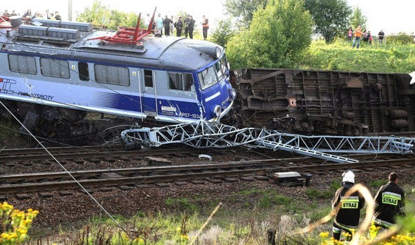 Wykolejona lokomotywa i jadący za nią wagon drugiej klasy przewrócony na bok.