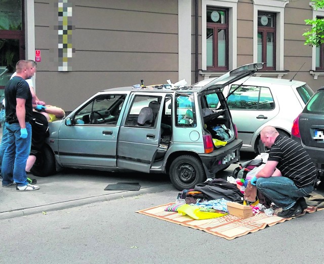 Kryminalni przeszukują auto 50-latka. Podejrzewany zakuty w kajdanki leży na masce swego auta.