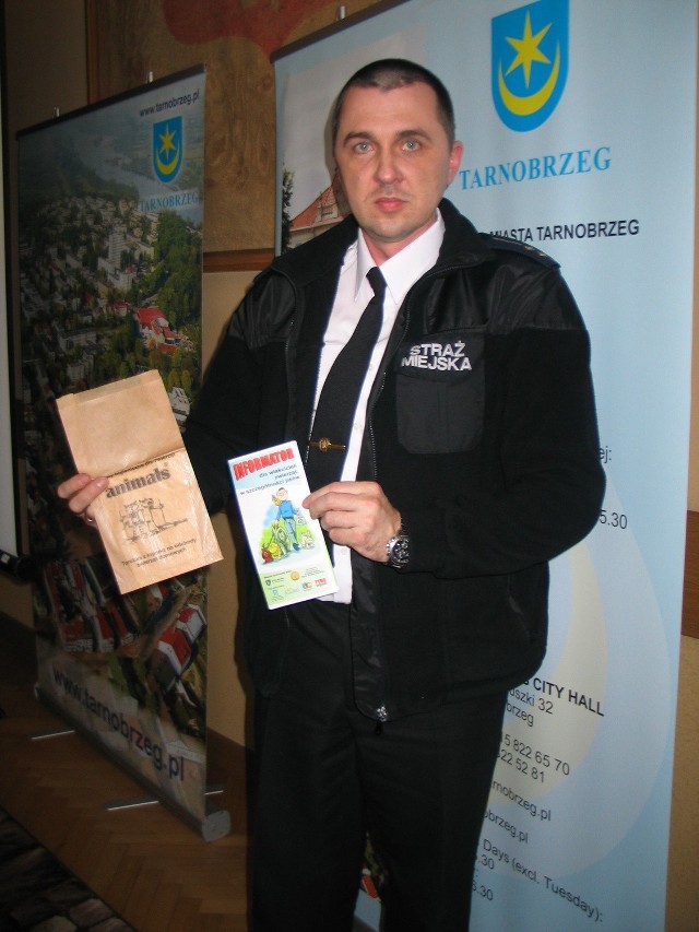 Robert Kędziora, po. komendanta Straży Miejskiej w Tarnobrzegu prezentuje ulotkę i darmowy pakiet, jakie przez najbliższe dni będą w ramach promocji rozdawane mieszkańcom spacerującym po mieście ze swoimi czworonogami.