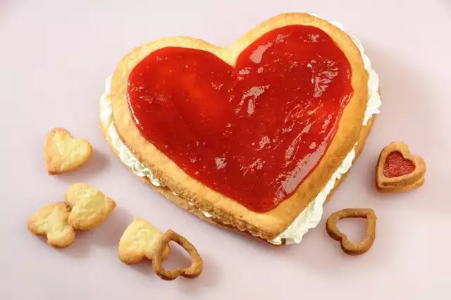 Serce na dłoniCóż lepiej wyrazić może nasze uczucia niż słodkie ciasto w kształcie serca. Jeżeli dodatkowo wypełnimy je marmoladą i pysznym kremem, idealny wieczór w towarzystwie naszej drugiej połówki gwarantowany.Składniki na ciasto:– kostka do pieczenia – 200 gramów,– mąka – 300 gramów,– cukier – 100 gramów,– żółtko – 2 sztukiSkładniki na krem:– kostka do pieczenia – 50 gramów,– budyń śmietankowy – 1 opakowanie,– mleko – 400 mililitrów,– twarda marmolada – 200 gramówSposób przygotowania:– Mąkę wymieszaj z cukrem, posiekaną margaryną do pieczenia i żółtkami.–Szybko zagnieć ciasto i odstaw na godzinę do lodówki.– Następnie ciasto rozwałkuj i wytnij z niego 4 identycznej wielkości serduszka.– Z pozostałego ciasta wytnij foremkami małe serduszka.– Duże serca przełóż na wyłożoną papierem do pieczenia blaszkę, nakłuj widelcem i piecz w 200 st. C około 15–20 minut.– Małe serduszka upiecz oddzielnie, gdyż pieką się krócej.– Budyń ugotuj na gęsto w 400 ml mleka.– Ostudź, a następnie zmiksuj z pozostałą margaryną do pieczenia.– Powstałym kremem posmaruj dwa serca i przykryj je dwoma pozostałymi.– Marmoladę włóż do rondla i lekko podgrzej, aby się rozpuściła.– Marmoladę wyłóż na ciasto i uformuj z niej serduszko.–Odstaw do zastygnięcia.