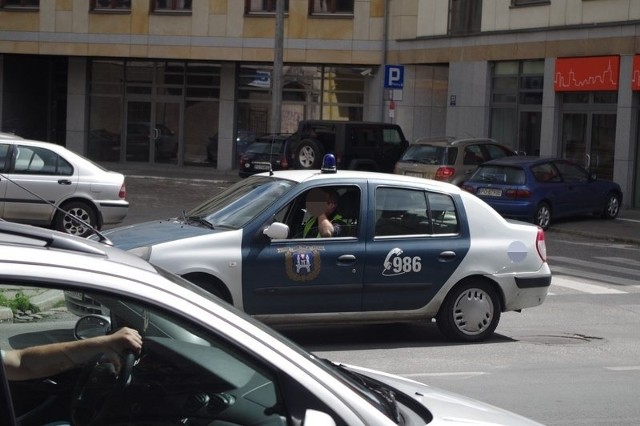 Strażnik miejski w służbowym samochodzie rozmawia przez telefon komórkowy prowadząc.