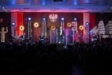 Koncert Bardów Wolności w historycznej sali BHP Stoczni Gdańskiej. Artyści na scenie, liczna publiczność na widowni