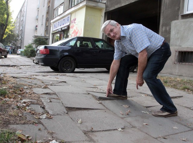 Pan Tadeusz, mieszkaniec bloku, wzdłuż którego ciągnie się chodnik, pokazuje zniszczenia.