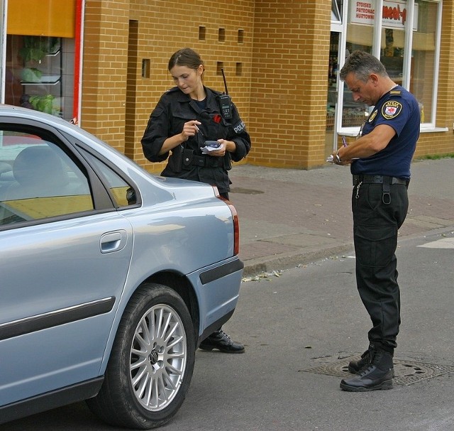 Słupscy strażnicy miejscy spisują numery rejestracyjne nieprawidłowo zaparkowanego samochodu.