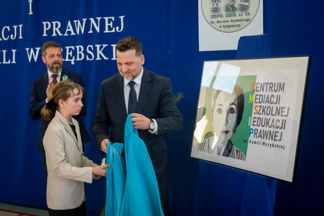 Mec. Jarosław Wyrębski z córką Tosią odsłaniają logo Centrum Mediacji Szkolnej i Edukacji Prawnej im. Kamili Wyrębskiej.