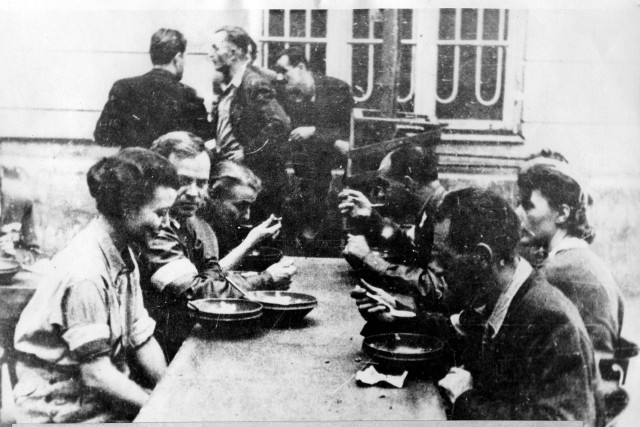 Powstańcy jedzą wspólny posiłek. Kliknij w obrazek, aby zobaczyć więcej zdjęć dotyczących kuchni w Powstaniu Warszawskim.