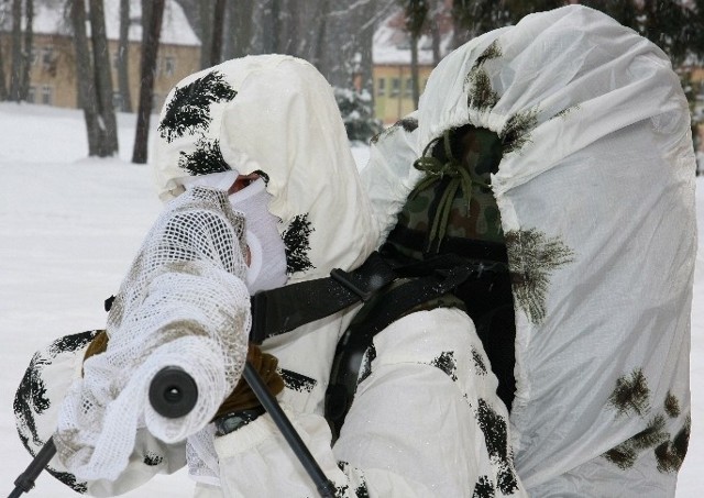 Snajper w kamuflażu zimowym. Uzbrojony w karabin TRG 22, z zasobnikiem na plecach. Jego ekwipunek i broń ważą 45 kg.