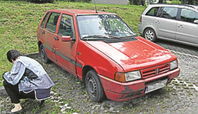 Fiat Uno pod blokiem nr 15 przy os. Niepodległości w Chrzanowie. Z jego kół dozorczyni wyrywa chwasty