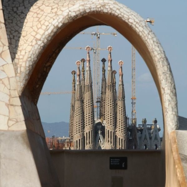 Kościół Sagrada Familia oglądany z pełnego łuków schodów i bajkowych kominów dachu kamienicy Casa Mila.