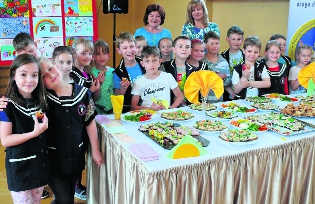 Prezes Batny Joanna Grobel-Proszowska, dyrektor szkoły Iwona Gałczyńska z dziećmi przy stole ze zdrowym jedzeniem.