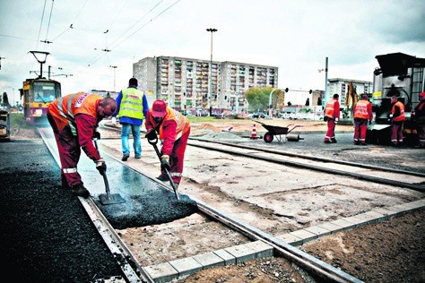 Na rondzie Inwalidów praca wre. Drogowcy leją asfalt pomiędzy szynami torowiska.