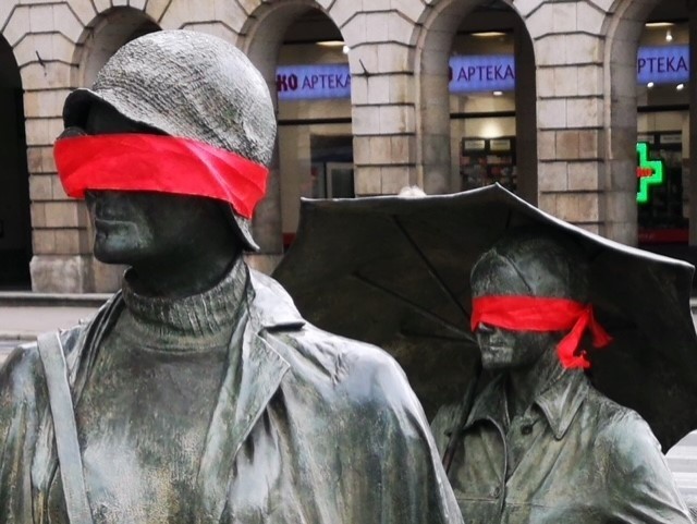 Czerwone opaski na figurach Pomnika Anonimowego Przechodnia...