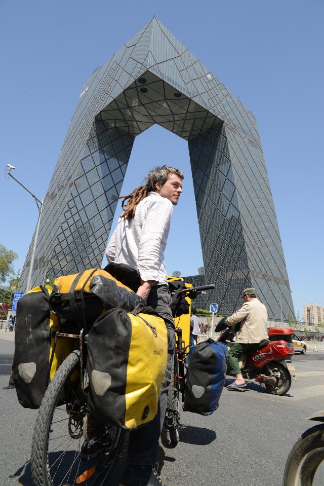 Adam W. Chałupski w Pekinie przed siedzibą Centralnej Telewizji Chińskiej. Oczywiście z nieodłącznym rowerem