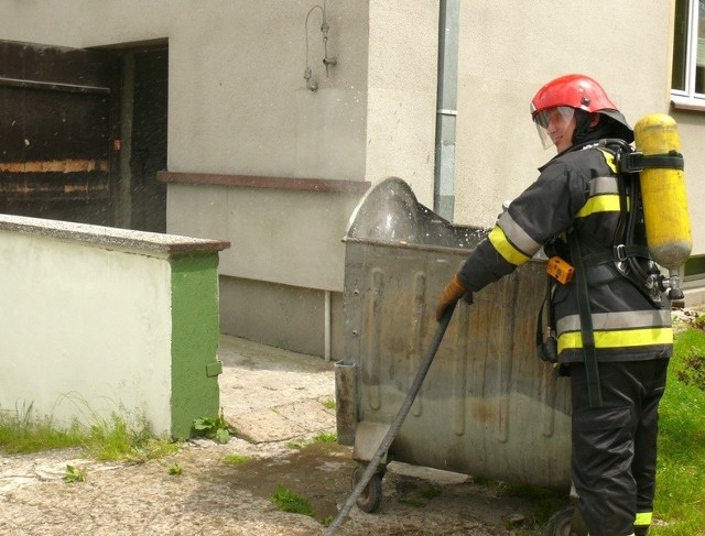 Strażak dogasza płonące śmieci w kontenerze ze zsypu.