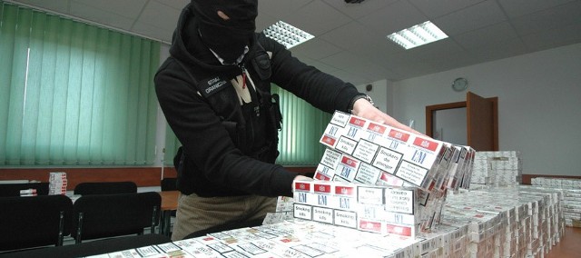 Zasłaniający oblicze funkcjonariusz kołobrzeskiej Placówki Straży Granicznej prezentuje zarekwirowane papierosy.